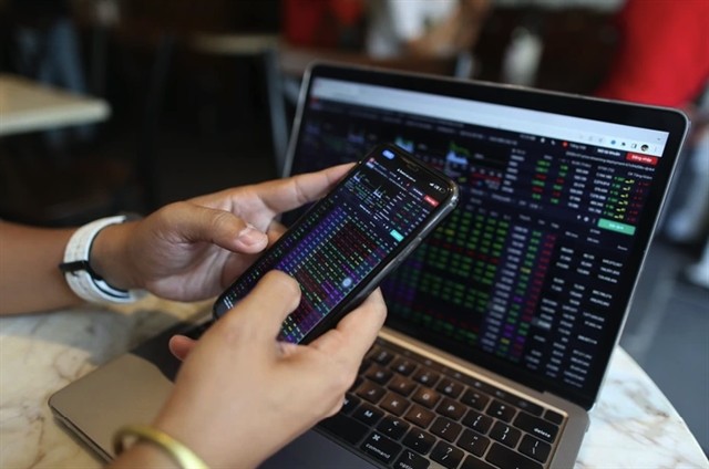 A mobile phone and laptop screen showing stock indices. The disparity in interest rate, monetary policies, volatile exchange rates and political fluctuations have significantly influenced foreign investors' actions. (Photo: VNA)